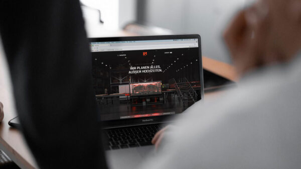 Laptop mit geöffneter MÖHLE-Website, auf der der Slogan „Wir planen alles. Außer Hochzeiten.“ auf einem dunklen Hintergrund mit Industriehalle angezeigt wird.